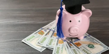 Piggy bank wearing a graduation cap on a stack of money, representing student loan refinancing for maximum savings.