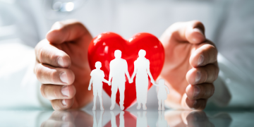 Hands protecting a paper cutout family and a red heart, illustrating the choice between term and whole life insurance for family security.