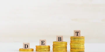 Debt strategy illustration: Growing stacks of coins with wooden blocks spelling "DEBT" to visualize debt payoff.