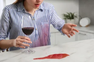 Pessoa segurando uma taça de vinho tinto com uma mancha acidental na camisa, ilustrando situações que exigem cuidados imediatos.